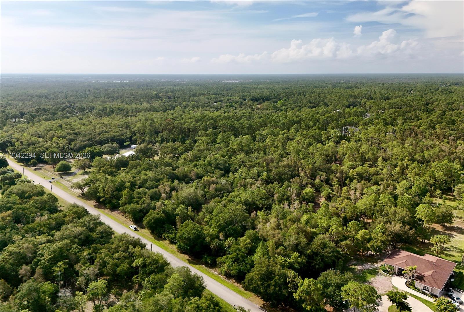 An aerial view shows a paved road running through a dense, wooded landscape — 280 35TH AVE NW, Naples FL 34120, NAPLES, FL