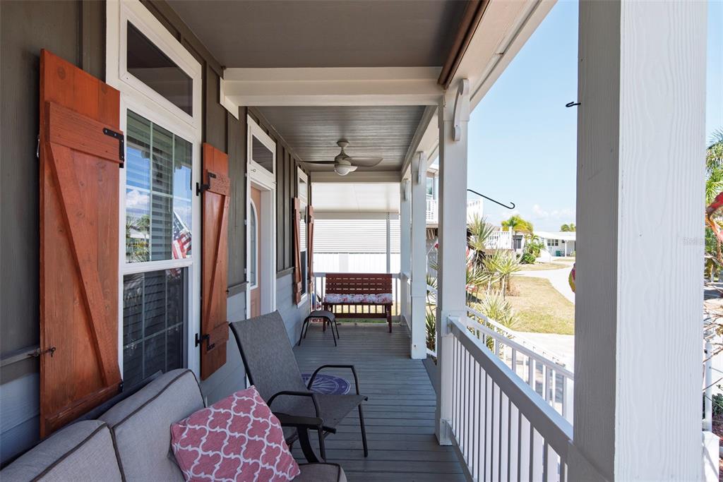 A covered porch features gray decking, a ceiling fan, outdoor seating, and white railings — 25 ALLIGATOR AVENUE, PUNTA GORDA, FL