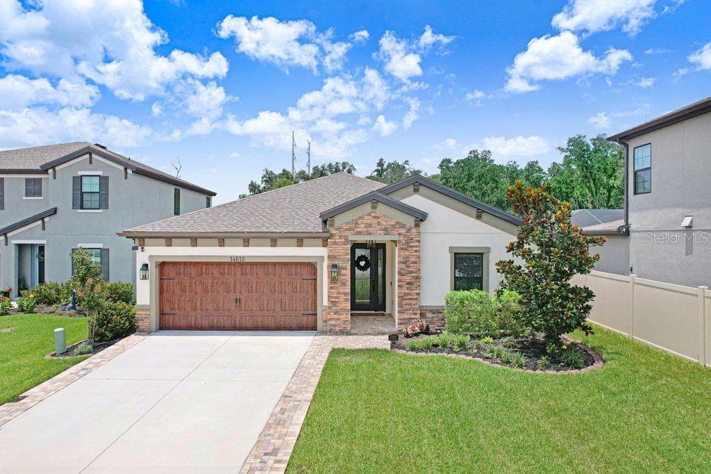 A single-story house with a stone-accented entryway, a wooden garage door, and a concrete driveway — 14610 HORSE TROT ROAD, LITHIA, FL