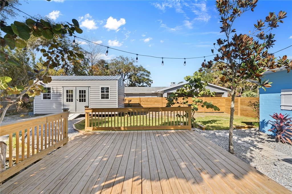 A wooden deck with railings overlooks a backyard featuring a shed and string lights — 1000 FAULKNER STREET, NEW SMYRNA BEACH, FL