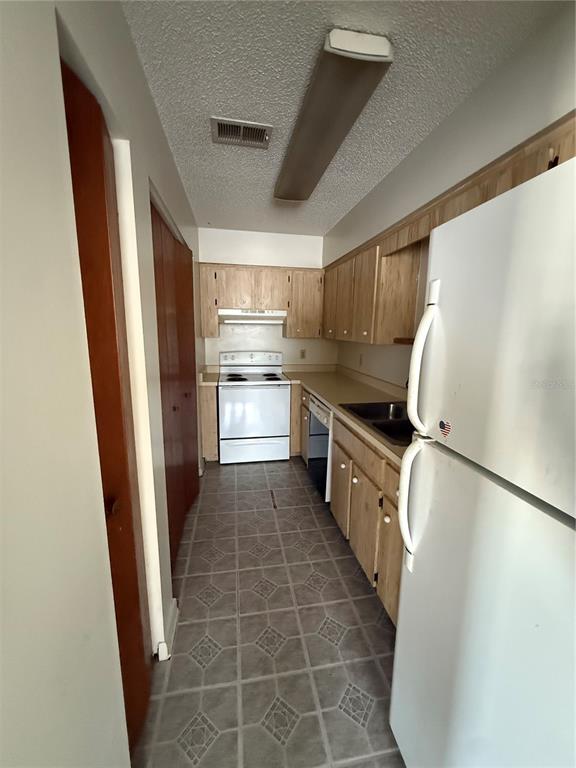 A galley kitchen features light wood cabinets, white appliances, and patterned vinyl flooring — 3032 SE 5TH TERRACE UNIT F, OCALA, FL