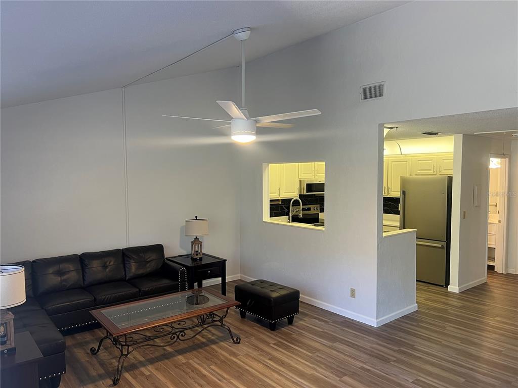 A living room with a black leather sofa, glass coffee table, and a kitchen pass-through window — 79 CYPRESS POND ROAD UNIT 79, PORT ORANGE, FL