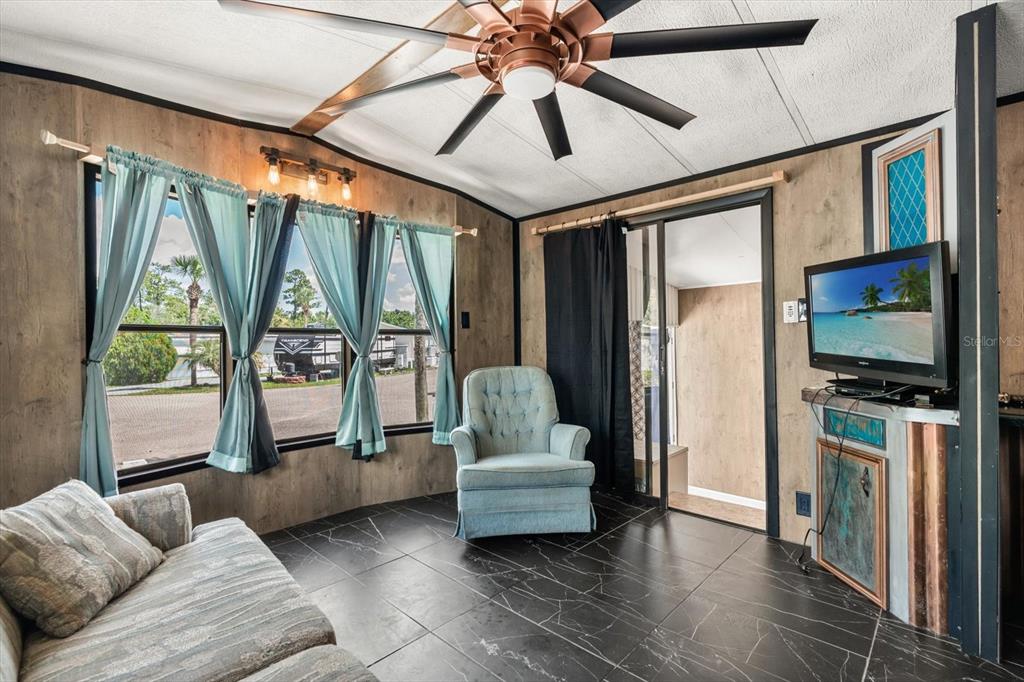 A living room features dark tile flooring, wood-paneled walls, a ceiling fan, and a television — 9000 US HIGHWAY 192 UNIT 11, CLERMONT, FL