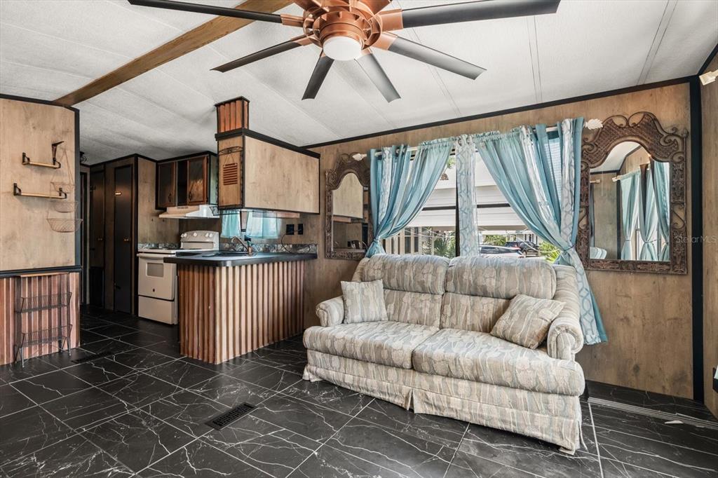 A living room with dark tile floors, wood-paneled walls, a sofa, and a ceiling fan — 9000 US HIGHWAY 192 UNIT 11, CLERMONT, FL