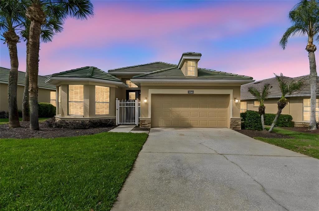 A single-story house with a green tile roof, tan stucco exterior, and a two-car garage — 13128 PALMILLA CIRCLE, DADE CITY, FL