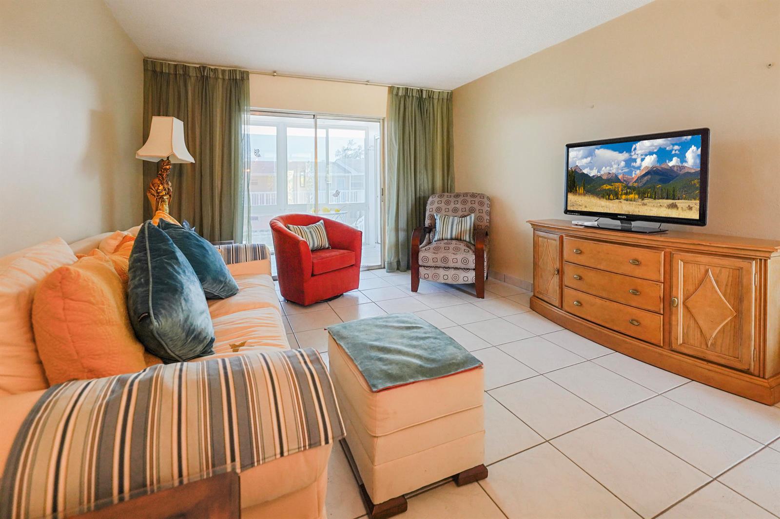 A living room with tile floors, a sofa, a red chair, and a television console — 2222 NE 1st Way # 204, Boynton Beach FL 33435, BOYNTON BEACH, FL