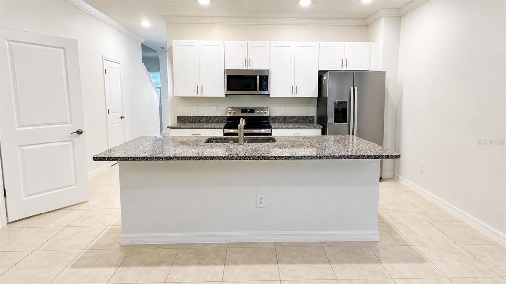 A kitchen features white cabinets, granite countertops, a central island, and stainless steel appliances — 9094 GALLANTREE PLACE, LAND O LAKES, FL