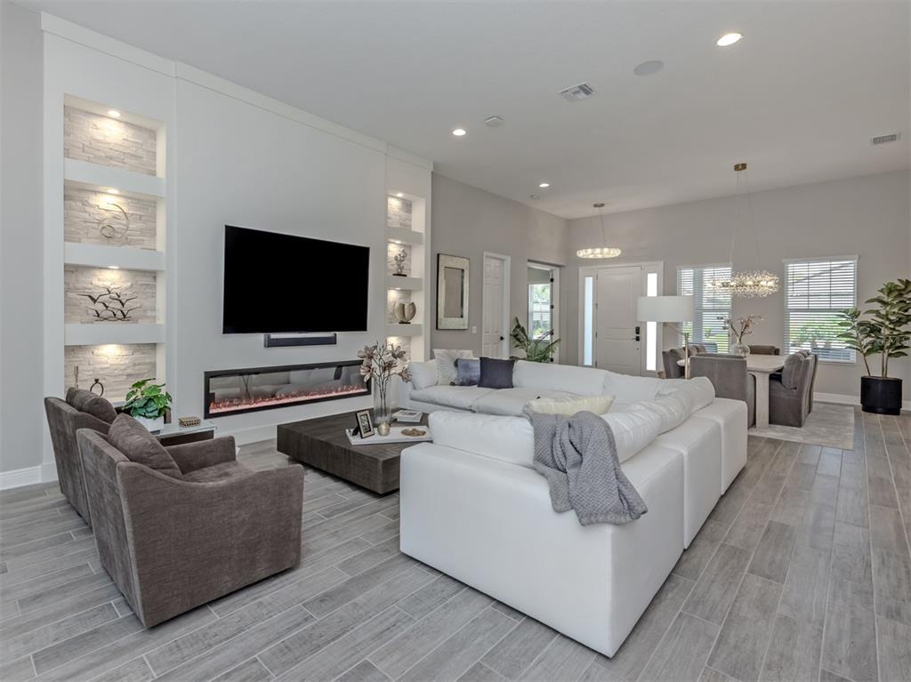 A modern living room features a white sectional, gray armchairs, and a linear fireplace — 19916 BRIDGETOWN LOOP, VENICE, FL