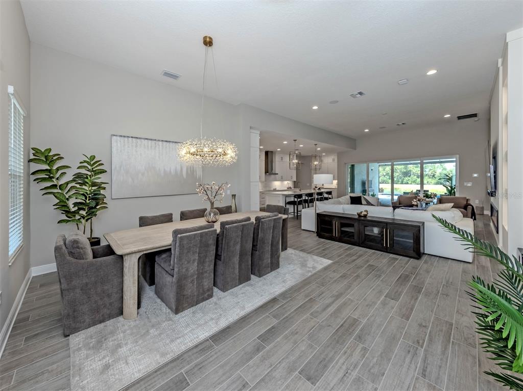 An open-concept dining and living area features gray wood-look tile flooring and a modern chandelier — 19916 BRIDGETOWN LOOP, VENICE, FL
