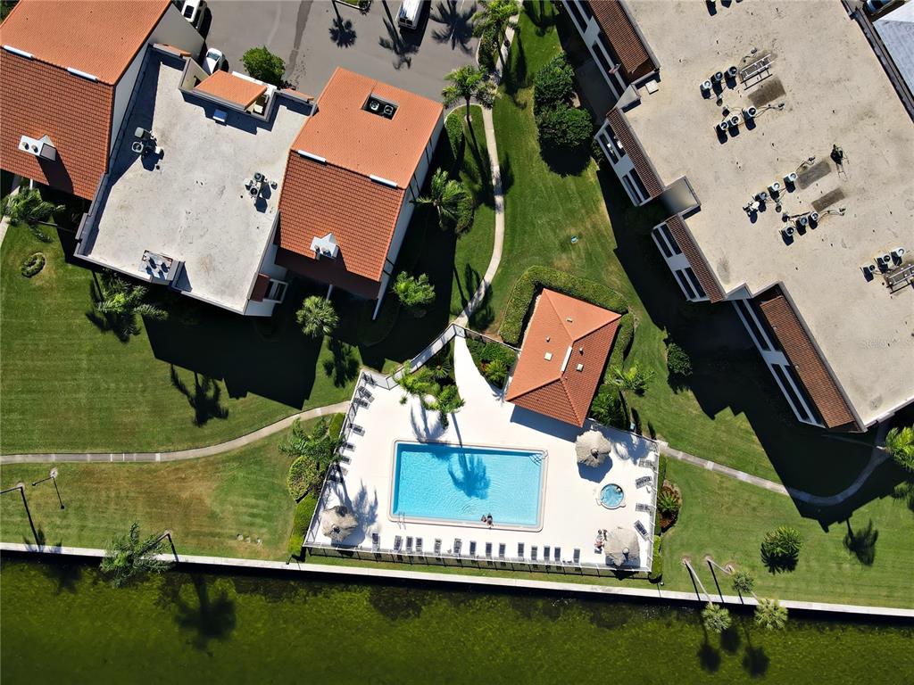 An aerial view shows a swimming pool and clubhouse nestled between apartment buildings near water — 103 1ST STREET E UNIT 113, TIERRA VERDE, FL