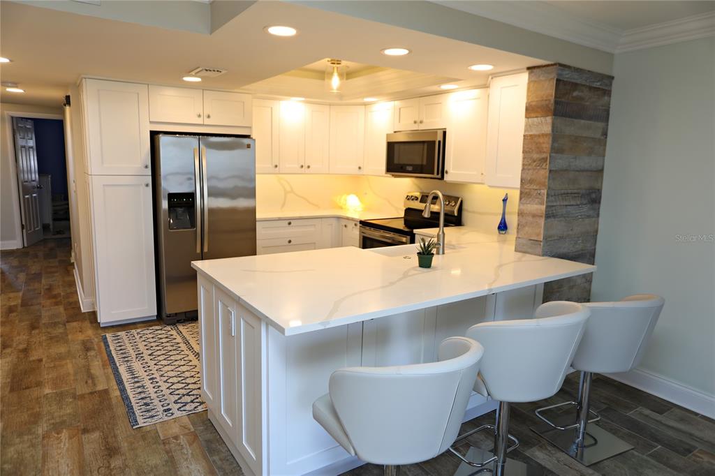 A kitchen features white cabinets, stainless steel appliances, a quartz island, and wood-look flooring — 103 1ST STREET E UNIT 113, TIERRA VERDE, FL