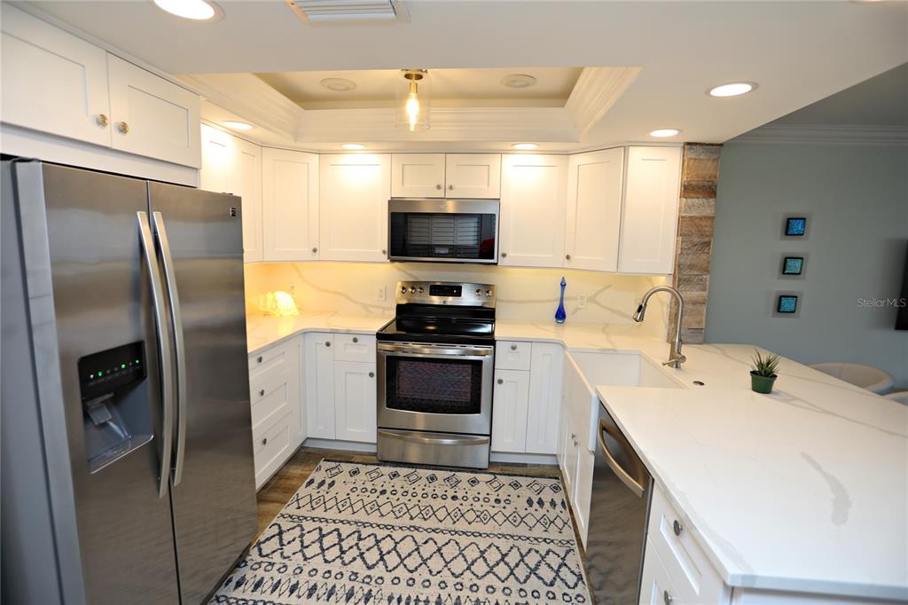 A kitchen features white cabinets, stainless steel appliances, quartz countertops, and a patterned area rug — 103 1ST STREET E UNIT 113, TIERRA VERDE, FL