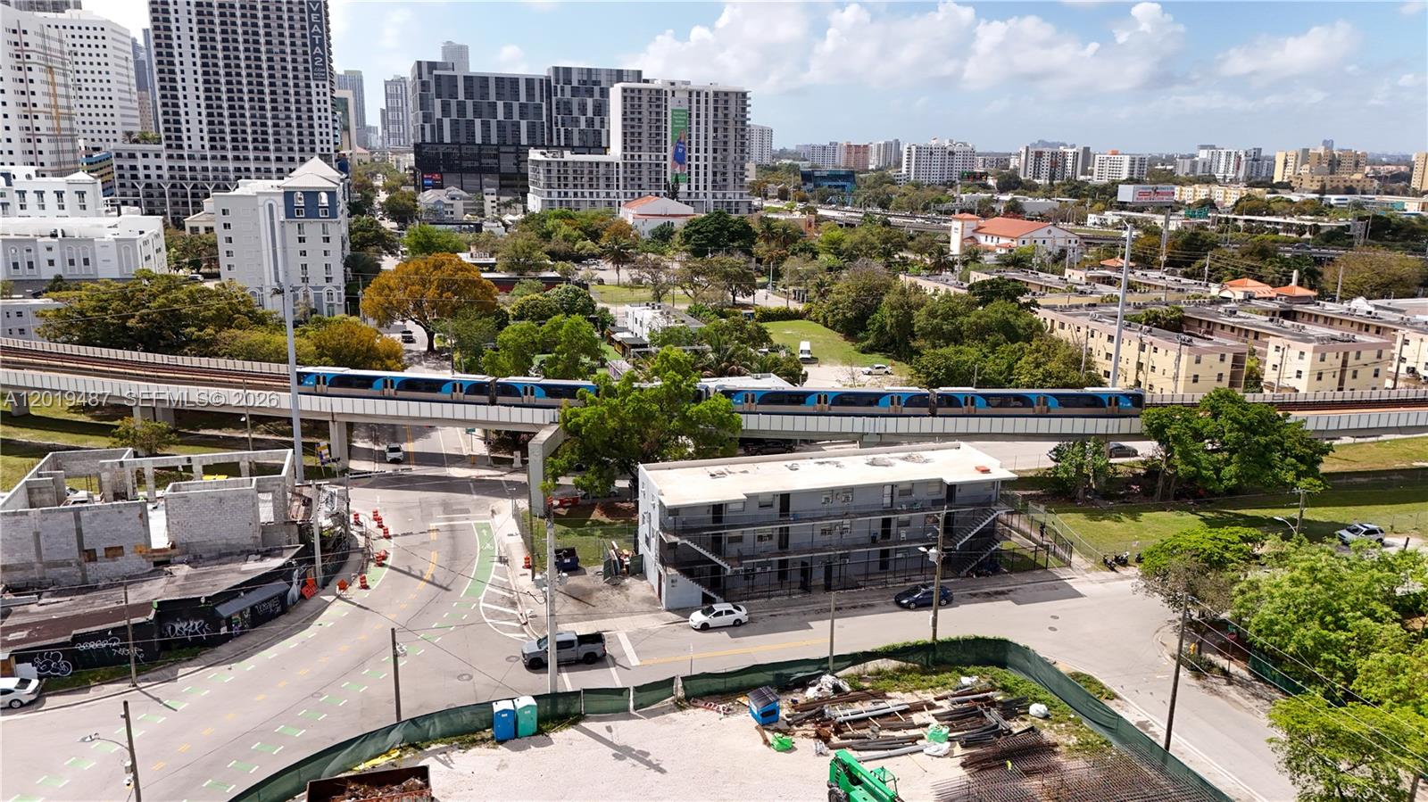 An elevated train travels along tracks above a city street with nearby buildings and construction — 220 NW 11th Ter, Miami FL 33136, MIAMI, FL