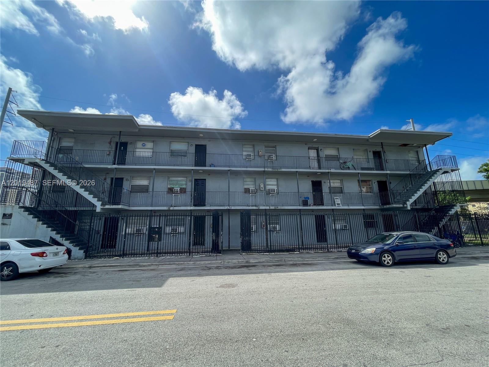 A three-story gray apartment building features exterior staircases and a black metal security fence — 220 NW 11th Ter, Miami FL 33136, MIAMI, FL