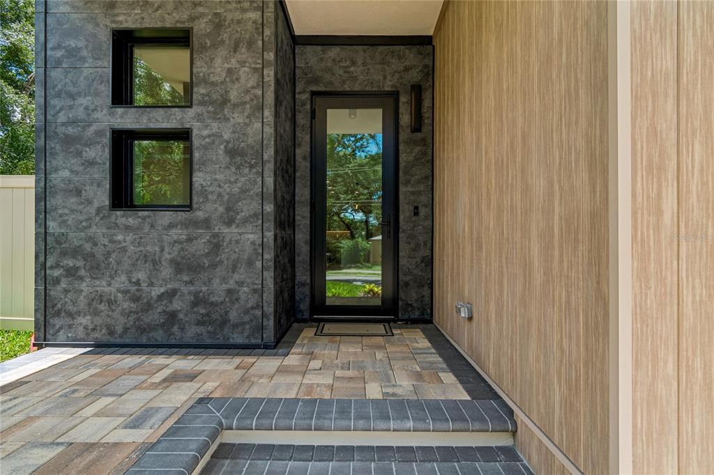 A modern entryway features a glass door, dark stone-look siding, and wood-paneled walls — 1305 HILTON PLACE, TAMPA, FL