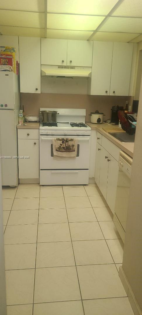 A kitchen features white cabinets, white appliances, and light-colored floor tiles — 18101 NW 68th Ave # C206, Hialeah FL 33015, HIALEAH, FL
