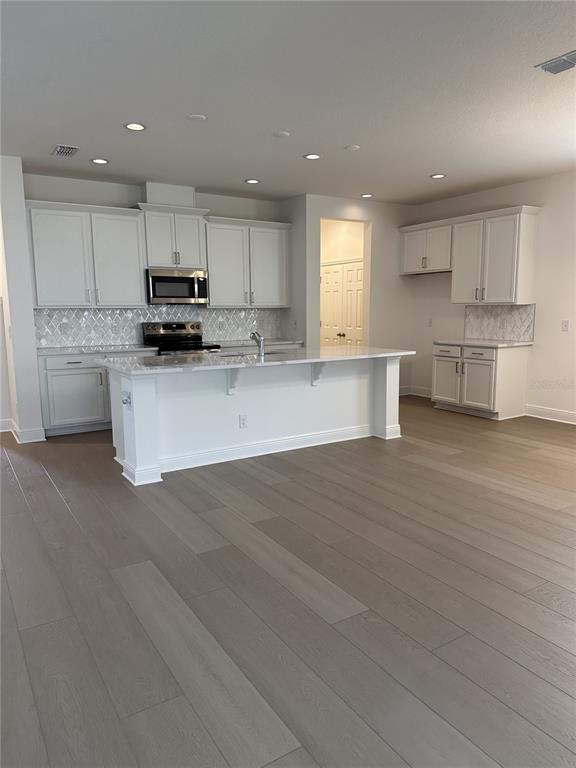 A modern kitchen features white cabinetry, a large island, and light wood-look flooring — 7737 SCICLI WAY, CLERMONT, FL