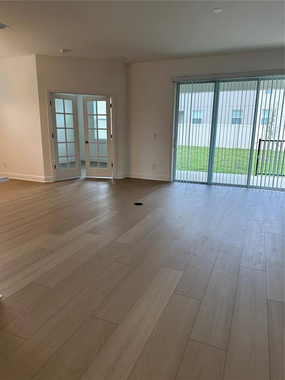 An empty room features light wood-look flooring, French doors, and a large sliding glass door — 7737 SCICLI WAY, CLERMONT, FL