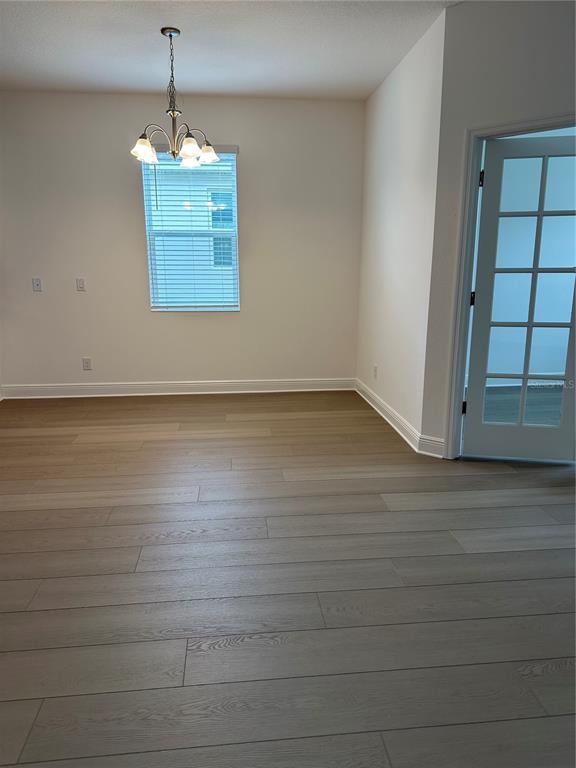 An empty room with light wood-look flooring, a chandelier, a window, and a glass-paneled door — 7737 SCICLI WAY, CLERMONT, FL