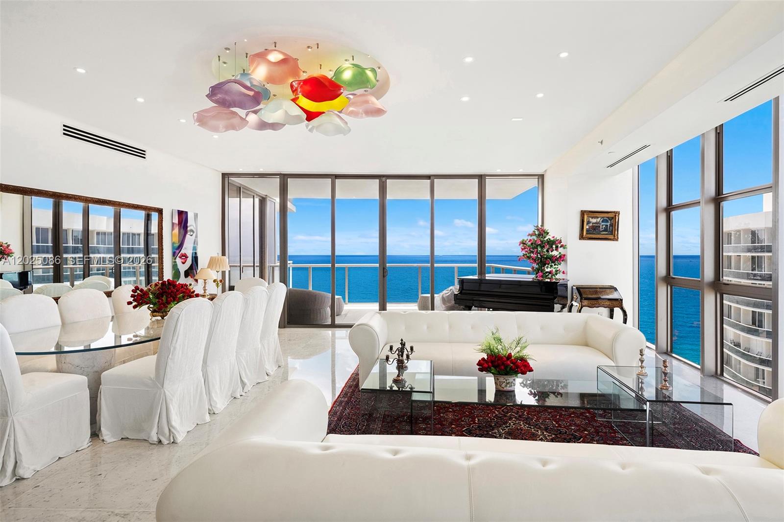 A bright living and dining room features white furniture, a colorful chandelier, and ocean views — 9701 Collins Ave # 2001S, Bal Harbour FL 33154, BAL HARBOUR, FL