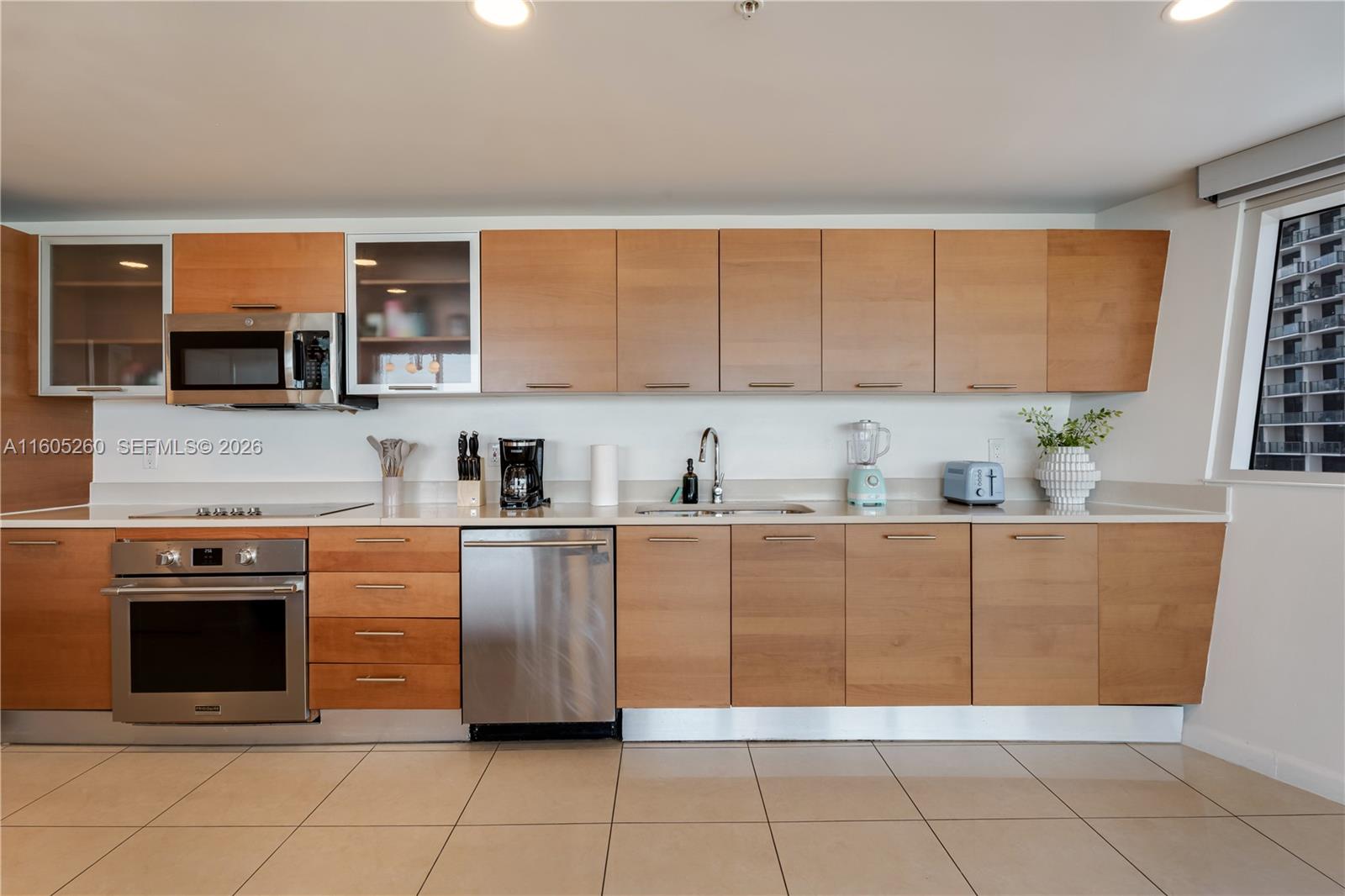 A kitchen features light wood cabinets, stainless steel appliances, and a window with a city view — 3250 NE 1st Ave # 715, Miami FL 33137, MIAMI, FL
