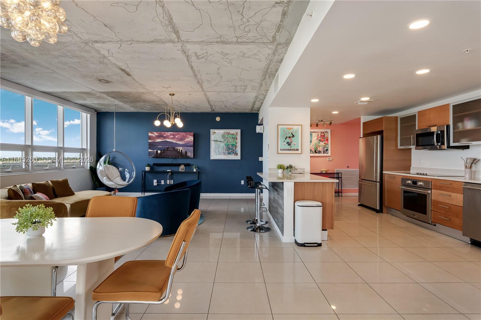 An open-concept living area features a concrete ceiling, blue accent wall, and modern kitchen — 3250 NE 1st Ave # 715, Miami FL 33137, MIAMI, FL