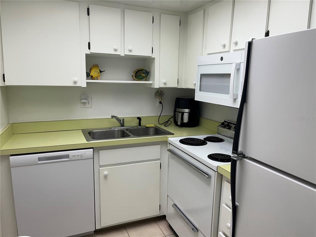 A small kitchen features white cabinets, a double sink, and white appliances — 612 BIRD BAY DRIVE S UNIT 112CAR, VENICE, FL