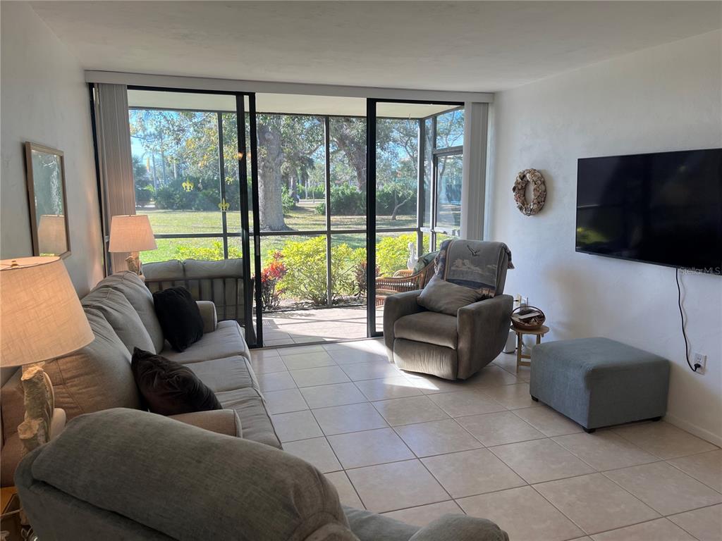 A living room with tile floors, a sofa, a recliner, and a screened-in patio view — 612 BIRD BAY DRIVE S UNIT 112CAR, VENICE, FL