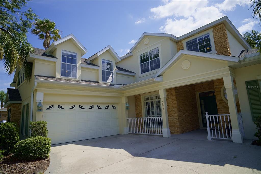 A two-story yellow house with a stone facade, a two-car garage, and a front porch — 6873 SCYTHE AVENUE, ORLANDO, FL