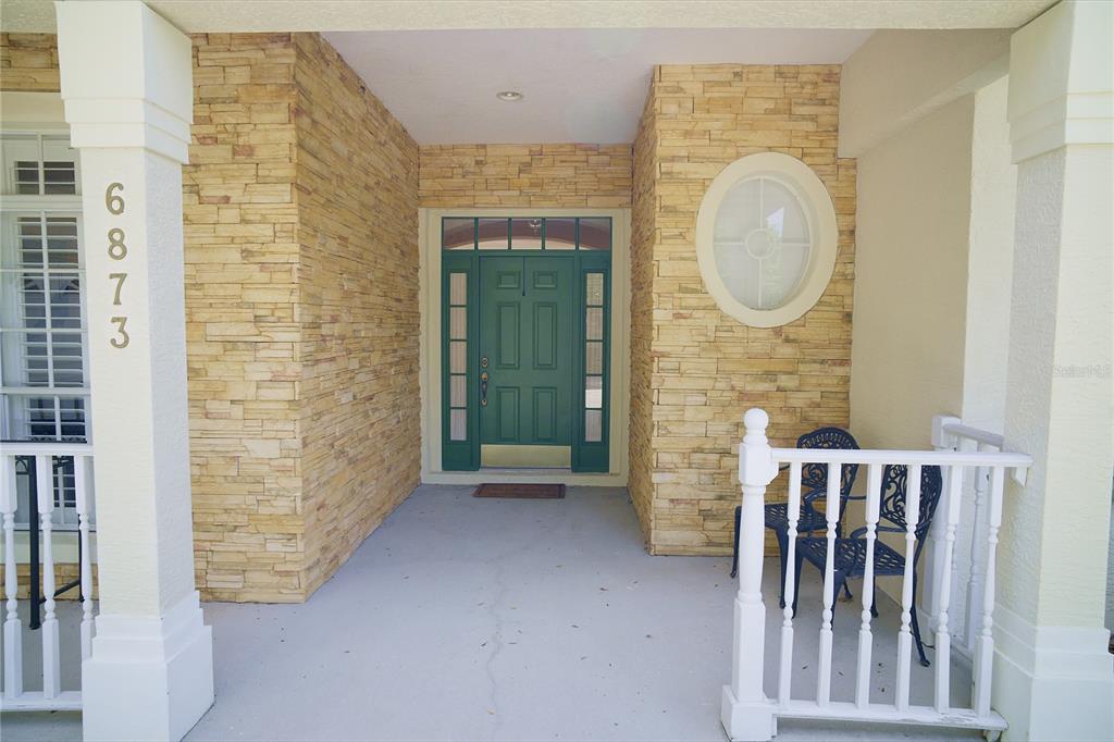 A covered front porch features stone veneer walls, a green double door, and white railings — 6873 SCYTHE AVENUE, ORLANDO, FL