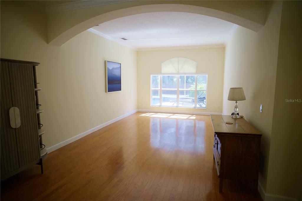 A bright, empty room with hardwood floors, a large arched opening, and a windowed wall — 6873 SCYTHE AVENUE, ORLANDO, FL