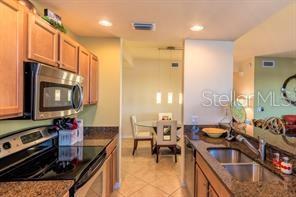A kitchen with wood cabinets, stainless steel appliances, and granite countertops overlooks a dining area — 7911 GRAND ESTUARY TRAIL UNIT 103, BRADENTON, FL