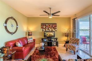 A living room features a red sofa, a patterned armchair, and a large wall clock — 7911 GRAND ESTUARY TRAIL UNIT 103, BRADENTON, FL