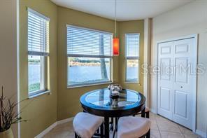 A dining nook features a glass-topped table, light-colored chairs, and large windows overlooking water — 7911 GRAND ESTUARY TRAIL UNIT 103, BRADENTON, FL