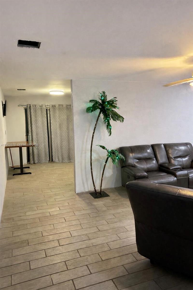 A living room features light tile flooring, a brown leather sofa, and an artificial palm tree — 10010 SW 161st St, Miami FL 33157, MIAMI, FL