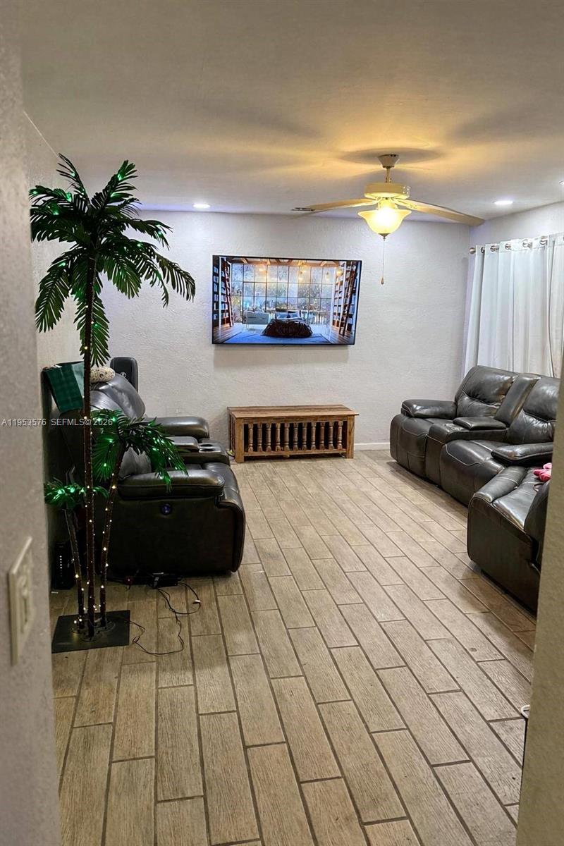 A living room features gray leather sofas, a wall-mounted television, and wood-look tile flooring — 10010 SW 161st St, Miami FL 33157, MIAMI, FL