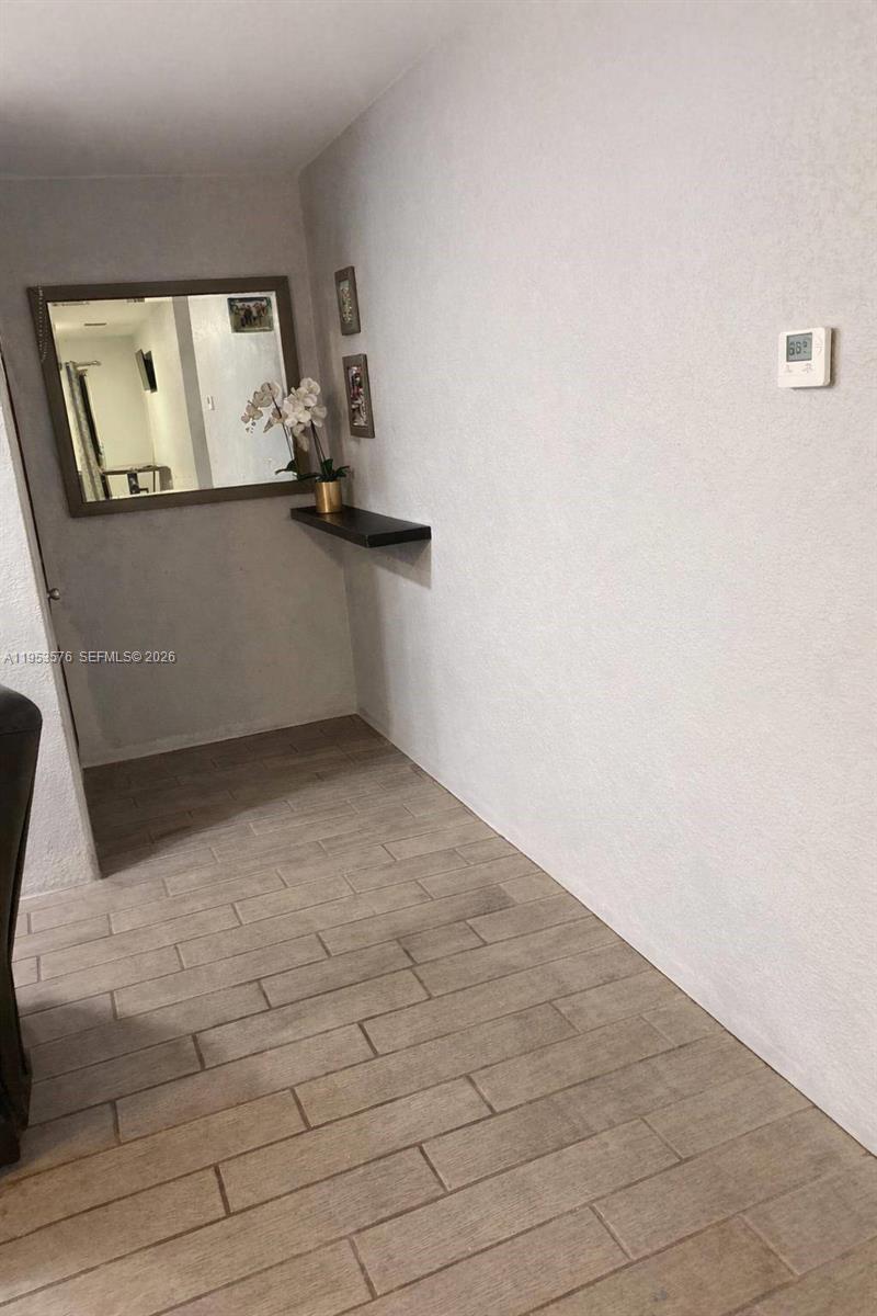 A hallway features light-colored wood-look tile flooring, a floating shelf, a mirror, and a thermostat — 10010 SW 161st St, Miami FL 33157, MIAMI, FL