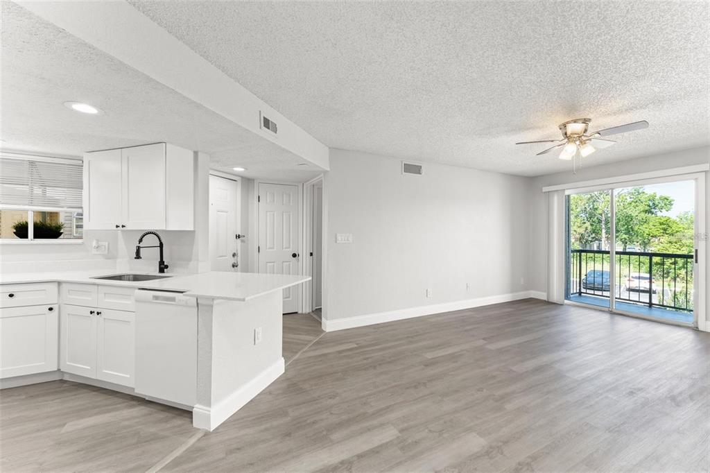 A bright kitchen with white cabinets and a dishwasher opens into a spacious living area — 1932 LAKE ATRIUMS CIRCLE UNIT 69, ORLANDO, FL