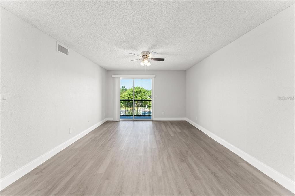 An empty living room features light gray wood-look flooring, white walls, and a sliding glass door — 1932 LAKE ATRIUMS CIRCLE UNIT 69, ORLANDO, FL