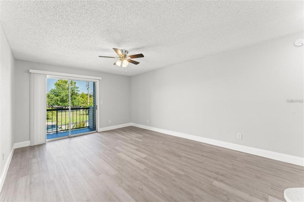 An empty room with light gray walls, wood-look flooring, a ceiling fan, and a sliding glass door — 1932 LAKE ATRIUMS CIRCLE UNIT 69, ORLANDO, FL