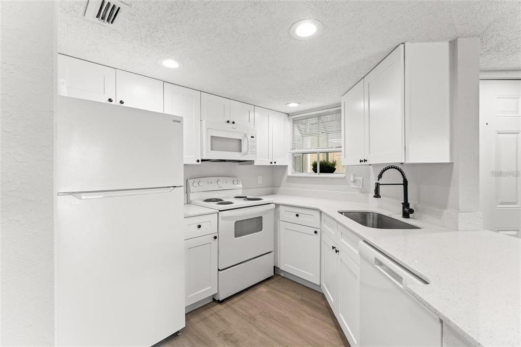 A white kitchen features white cabinetry, a white stove, a refrigerator, and a dark faucet — 1932 LAKE ATRIUMS CIRCLE UNIT 69, ORLANDO, FL