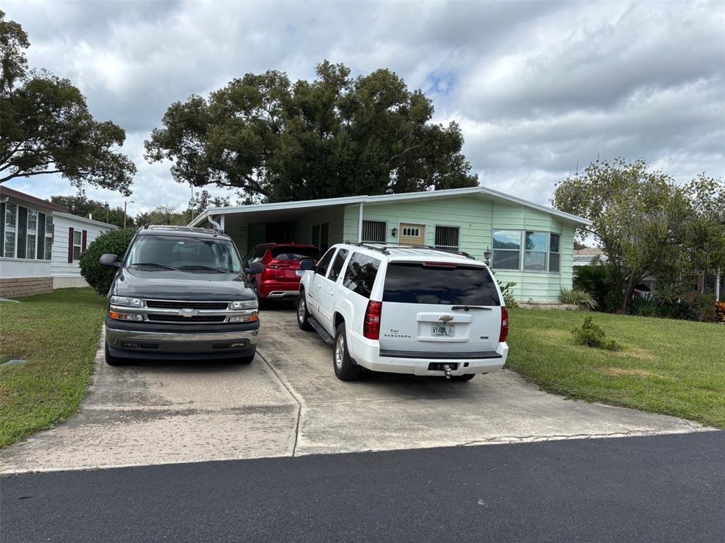 A light green mobile home with a carport and three parked vehicles in the driveway — 6033 GRAND OAKS DRIVE SE, WINTER HAVEN, FL