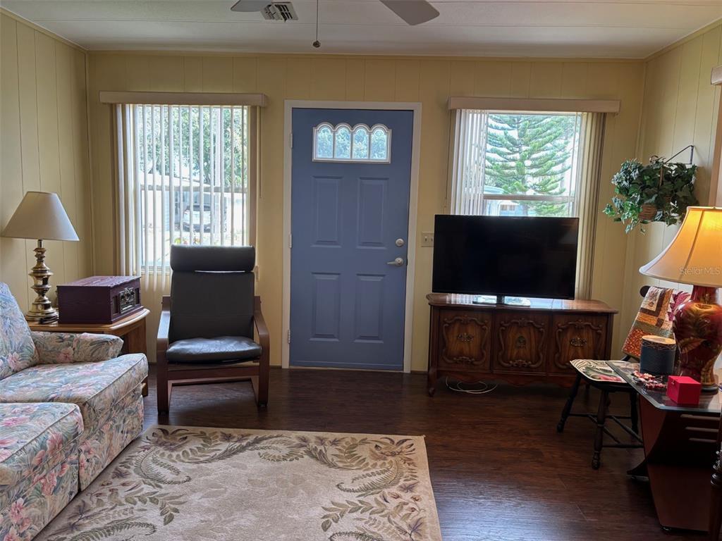 A living room features a blue front door, wood-look flooring, and a floral sofa — 6033 GRAND OAKS DRIVE SE, WINTER HAVEN, FL