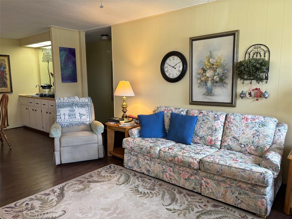 A living room features a floral sofa, a recliner, and a wall clock on yellow walls — 6033 GRAND OAKS DRIVE SE, WINTER HAVEN, FL