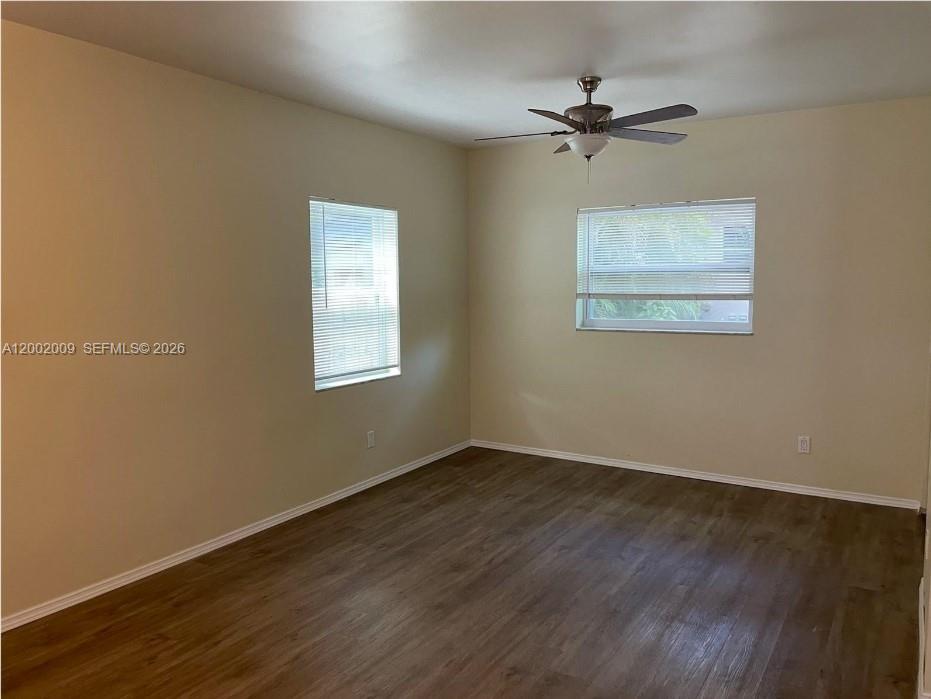 An empty room features beige walls, wood-look flooring, two windows with blinds, and a ceiling fan — 1720 Pierce St # 1, Hollywood FL 33020, HOLLYWOOD, FL