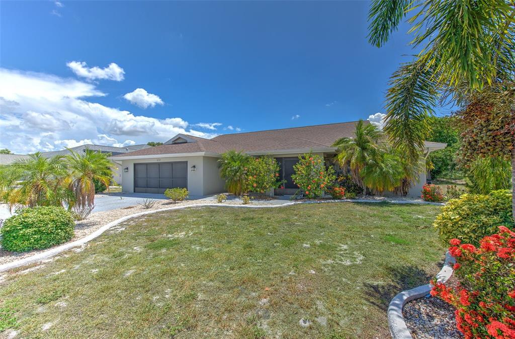 A single-story house with a garage, palm trees, and a landscaped yard under a blue sky — 1812 NEW BEDFORD DRIVE, SUN CITY CENTER, FL
