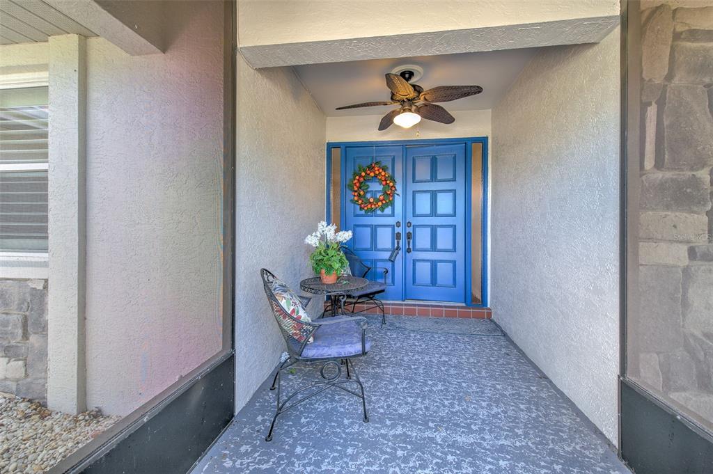 A covered front porch features a blue double door, a ceiling fan, and patio furniture — 1812 NEW BEDFORD DRIVE, SUN CITY CENTER, FL