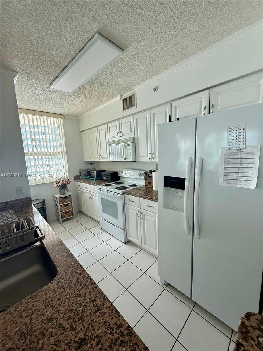 A kitchen features white cabinets, granite countertops, a white refrigerator, and a tiled floor — 1155 Brickell Bay Dr # 1702, Miami FL 33131, MIAMI, FL