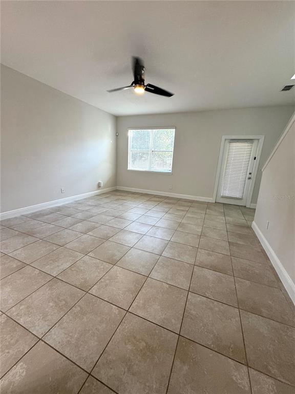 An empty room features light-colored walls, large square floor tiles, a ceiling fan, and a door — 12784 GARRIDAN AVENUE, WINDERMERE, FL