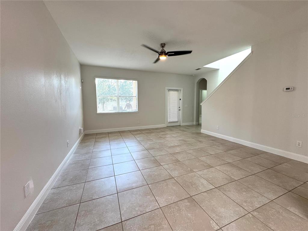 An empty living room features light-colored tile flooring, a ceiling fan, and a sliding glass door — 12784 GARRIDAN AVENUE, WINDERMERE, FL
